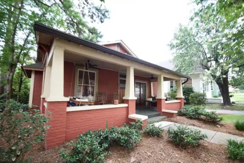 A charming red house with a porch, surrounded by greenery and trees, showcasing a welcoming entrance.