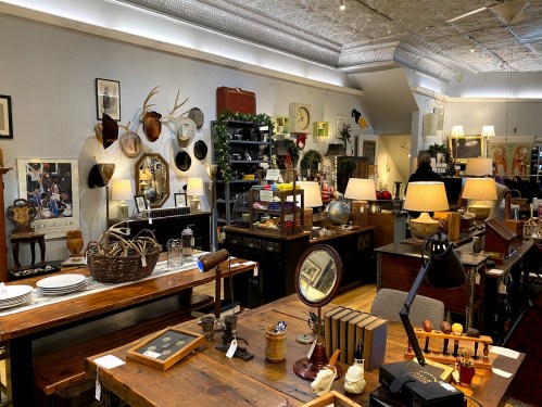A cozy antique shop filled with wooden furniture, vintage decor, and various collectibles, illuminated by warm lighting.