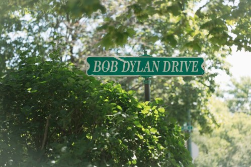 A green street sign reading "Bob Dylan Drive" surrounded by lush greenery.
