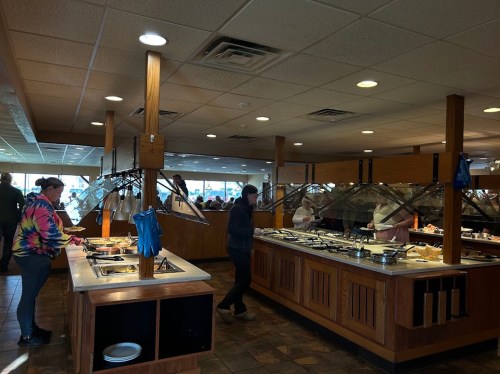 A busy buffet restaurant with diners serving themselves from a variety of food stations. Bright and spacious interior.