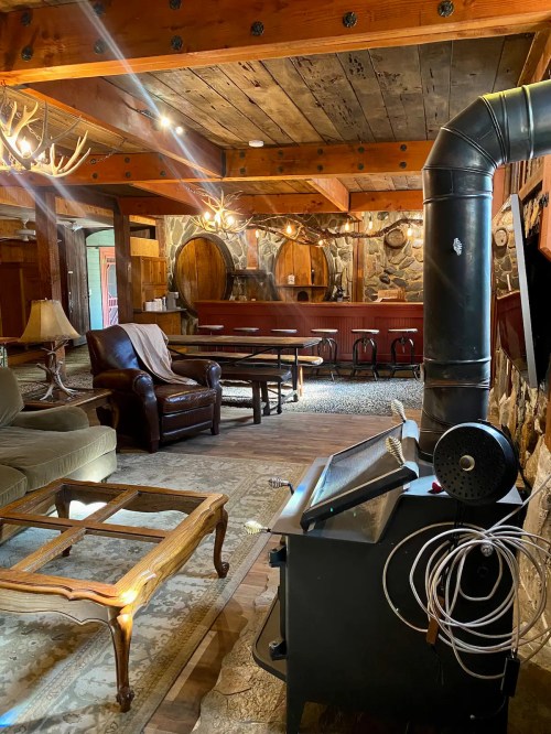 Cozy rustic interior with wooden beams, leather armchair, stone walls, and a wood stove, creating a warm atmosphere.