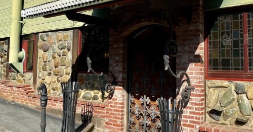 A brick and stone building entrance with decorative ironwork and stained glass windows.
