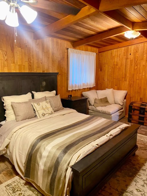 Cozy bedroom with wooden walls, a bed with striped bedding, a sofa, and warm lighting.