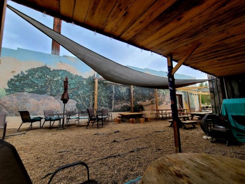 A cozy outdoor space with a mural, picnic tables, and a shaded area under a wooden structure.