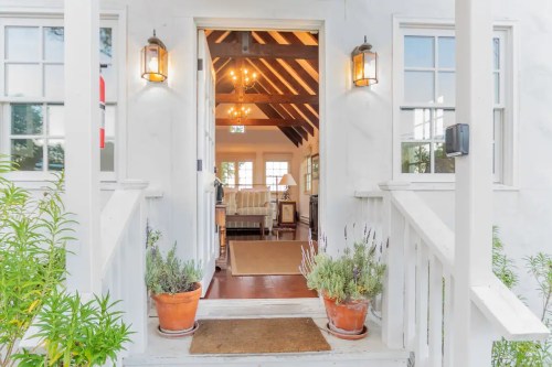 A welcoming entrance with potted plants, leading into a bright, airy interior with wooden beams and warm lighting.