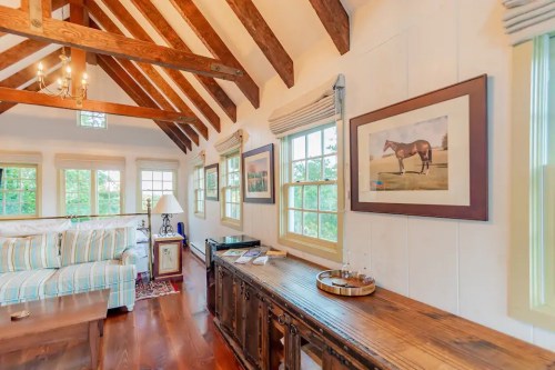 Cozy interior with wooden beams, a striped sofa, and framed artwork, featuring large windows and warm lighting.