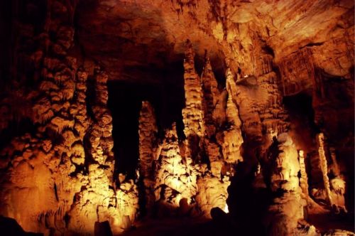 Stalactites and stalagmites illuminated in a dark cave, showcasing intricate rock formations.