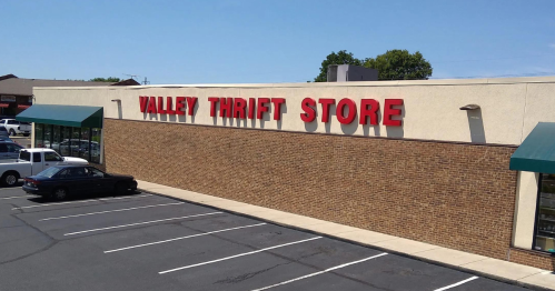 Exterior of Valley Thrift Store with a brick facade and red signage, featuring a clear blue sky above.