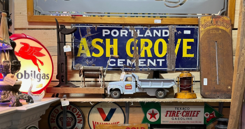 A collection of vintage items, including a cement sign, toy truck, and various old gas station signs on a wooden shelf.