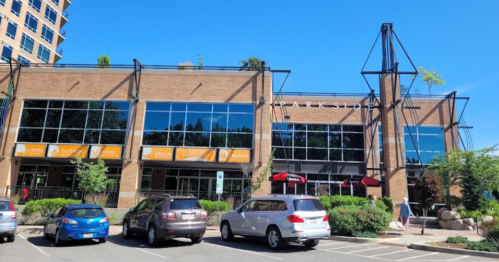 Exterior of a brick building with large windows, featuring "PARKSIDE" signage and outdoor seating. Clear blue sky above.