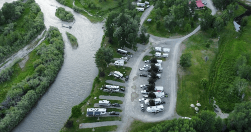 Aerial view of an RV park near a winding river, surrounded by greenery and trees.