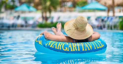 A person relaxes on a blue inflatable tube in a pool, wearing a wide-brimmed straw hat.