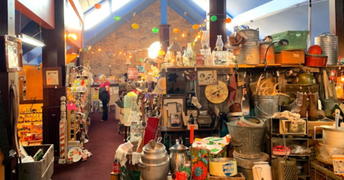 A cozy antique shop filled with various vintage items, decorations, and warm lighting, with a person browsing in the background.