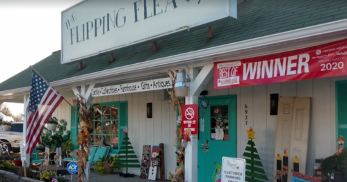 A storefront with a sign reading "The Flipping Flea," featuring decorations, an American flag, and a "Best of" winner banner.