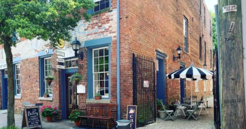 Charming brick building with a café entrance, outdoor seating, and striped awning in a quaint alleyway.