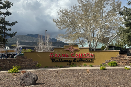 grand canyon railway & hotel sign with a train and mountains in the background