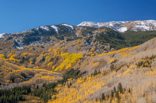 A serene mountain landscape with vibrant autumn trees reflecting in a calm lake under a clear blue sky in Colorado