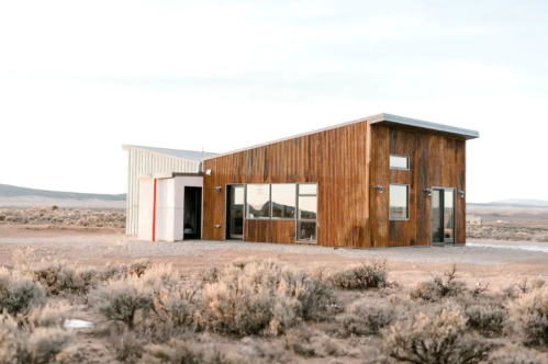 Modern wooden house in a desert landscape, featuring large windows and a minimalist design.