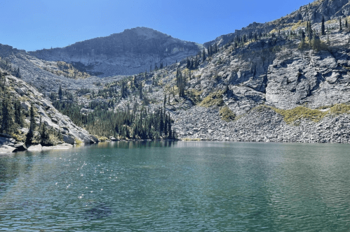 A serene lake surrounded by rocky mountains and lush trees under a clear blue sky.