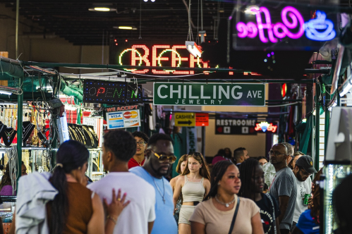 A bustling market scene with people walking, jewelry shops, and neon signs, including "CHILLING AVE" and "RESTROOM."