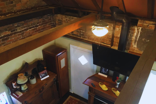 A cozy room with exposed brick walls, wooden beams, a ceiling fan, and a TV on a wooden cabinet.