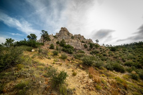 A rocky hillside with sparse vegetation under a cloudy sky, showcasing rugged cliffs and a natural landscape.