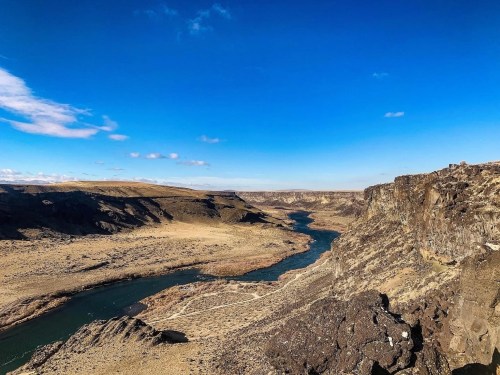 A scenic view of a winding river surrounded by rocky cliffs and arid landscape under a clear blue sky.