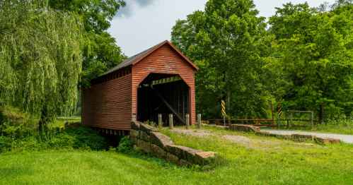a small rustic red covered bridge surrounded by greenery in west virginia