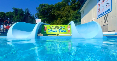 A bright blue water slide at Yawgoo Valley Water Park, with a sunny sky and trees in the background.