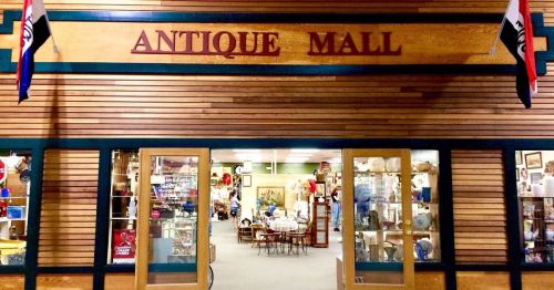Entrance of an antique mall featuring wooden signage and displays of vintage items visible through the glass doors.