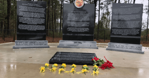 Memorial site with black stone plaques and flowers, surrounded by trees, honoring fallen individuals.