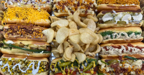 A variety of gourmet hot dogs topped with different ingredients, surrounded by crispy potato chips.