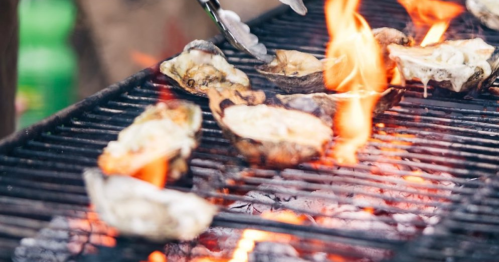 Grilled oysters on a barbecue grill with flames and smoke rising.