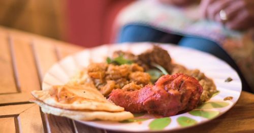 A plate of colorful Indian food featuring chicken, lentils, and naan on a wooden table.