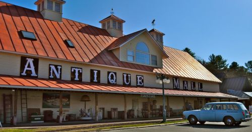 A vintage antique mall with a red roof and large letters, featuring a classic car parked in front.