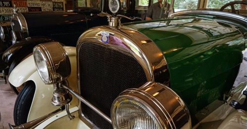Close-up of a vintage green car with chrome details and a classic headlight, displayed in a garage.