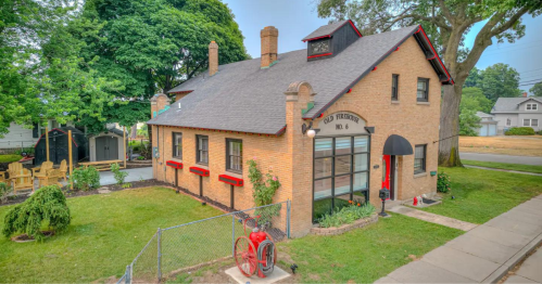 A charming brick building with a large window, surrounded by greenery and a vintage fire hydrant in the foreground.