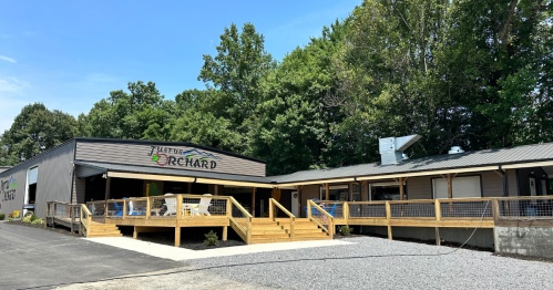 A modern building with a wooden deck, surrounded by trees, featuring a sign that reads "Just Orchard."