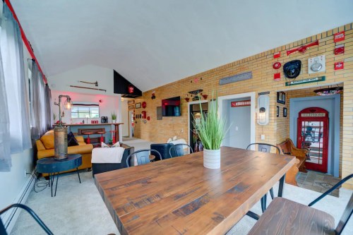 Cozy living space with a wooden dining table, yellow couch, and vintage decor on brick walls. Bright and inviting atmosphere.