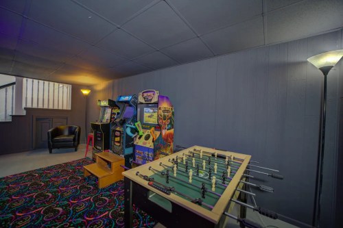 A cozy game room featuring arcade machines, a foosball table, and a comfortable chair on a colorful carpet.
