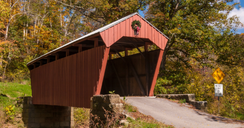 A red covered bridge with a Christmas wreath surrounded by lush greenery in West Virginia