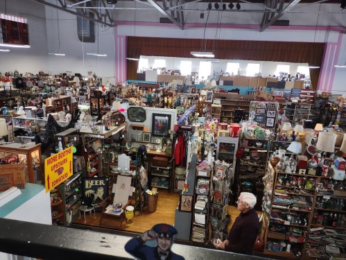 A bustling antique store filled with various collectibles, furniture, and decor, with a man browsing in the foreground.