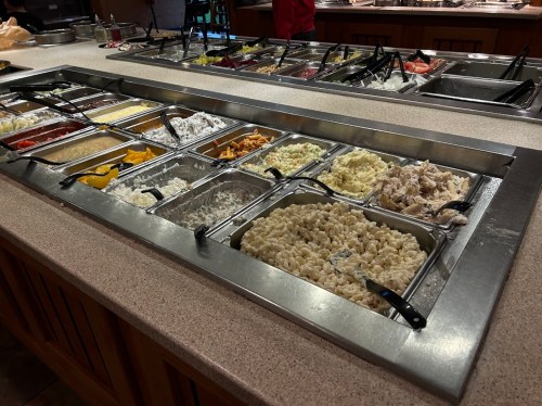 A buffet-style food station with various trays of pasta, sauces, and toppings arranged neatly on a countertop.