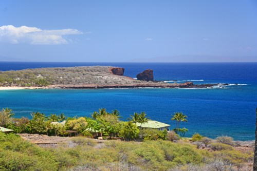 Scenic coastal view featuring rocky formations, clear blue water, and lush greenery under a bright sky.