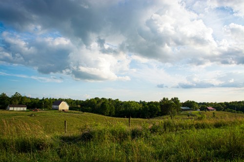 Rural eastern Ohio landscape of rolling hills and farmsteads with dramatic clouds in the sky.