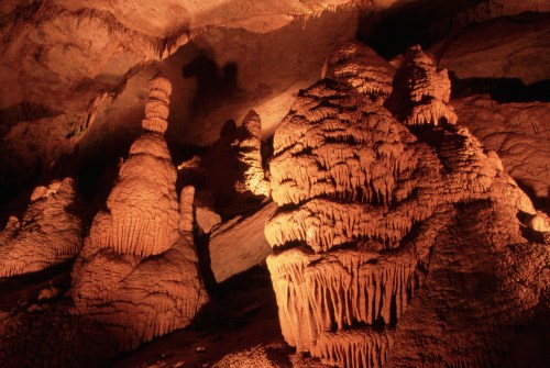 Stalactites and stalagmites illuminated in a cave, creating dramatic shadows and textures on the rocky surfaces.