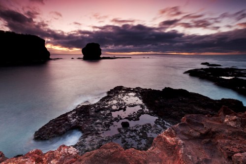 Serene coastal landscape at sunset, featuring rocky shorelines and calm waters under a colorful sky.
