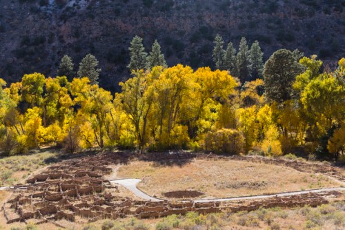 Aerial view of ancient ruins surrounded by vibrant autumn trees and a winding path in a mountainous landscape.