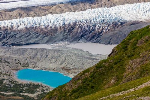 A stunning landscape featuring a glacier, a turquoise lake, and a grayish body of water surrounded by rocky terrain.