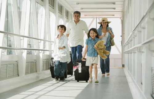 A family of four walks down a corridor, carrying luggage and a stuffed animal, smiling and enjoying their time together.